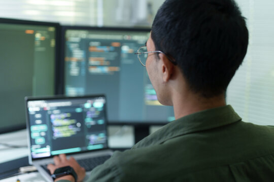 Male developer writing code on multiple monitors