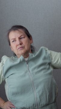 Middle aged woman warms up with repeated side bends against neutral studio wall. Woman lifts arm high and shifts torso, showing steady balance and quiet determination in simple activewear.