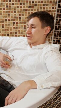 Sad and lonely young caucasian male in a white shirt lying in a bathtub, experiencing a hangover and emotional distress while drinking whiskey, symbolizing alcohol abuse and depression