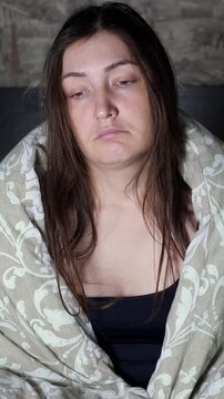 Young sleepy woman with messy hair wrapped in a blanket just woke up. Drowsy, exhausted female yawning and trying to get out of bed in the morning after a sleepless and restless night