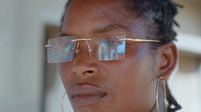 Close up on face details including eyeglasses and hoop earrings. Soft lighting highlights skin texture while background remains blurred. Shot maintains focus on facial features