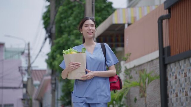 A healthcare worker walks through a neighborhood holding a grocery bag filled with fresh vegetables after completing home visits, conveying a sense of daily routine and self care.