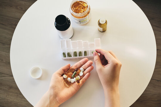 Hands arranging different medications and vitamins into weekly pill dispenser for health management