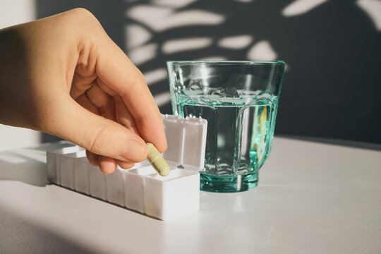Woman taking capsule from pill organizer with glass of water