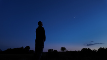 Fototapeta premium Silhouette of a person in nature observing night sky, Moon, stars and planets from a remote location.