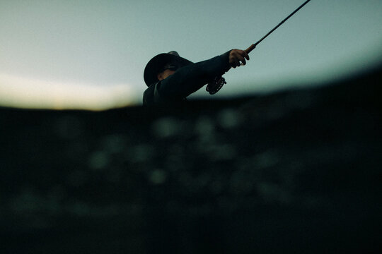 Fly fisherman casts across the river in fading evening light.