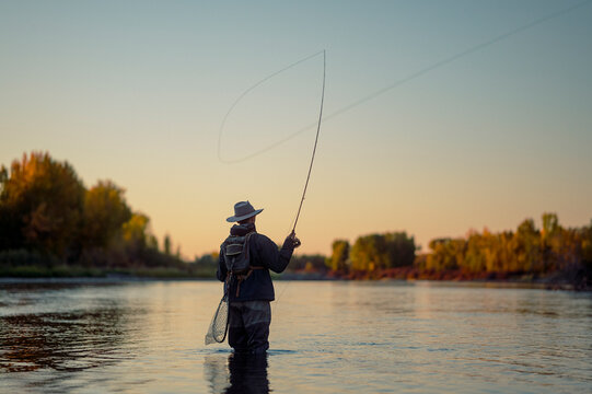 Fly fisherman casts a looping line while standing in a wide river.