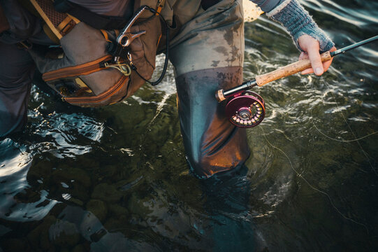 Close view of a fly rod and reel beside an angler standing in water.