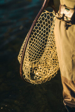 Fishing net hangs beside an angler standing in shallow river water.