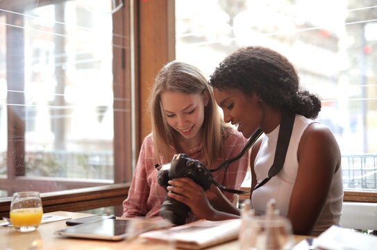 Two young women are using a digital camera in a caf&eacute;.