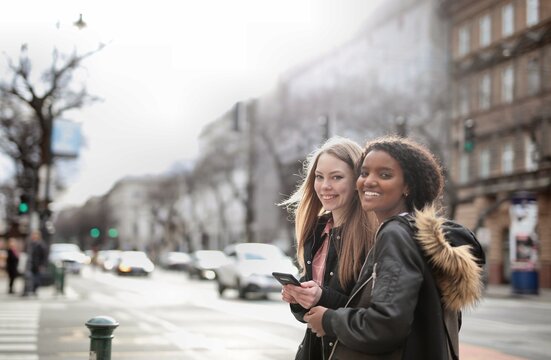 Two young women on the street are using a smartphone.
