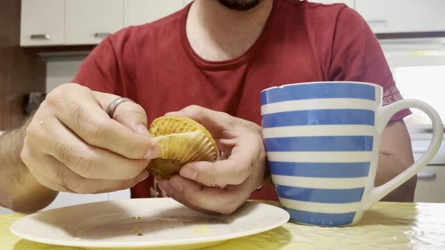 Magdalena quitando c&aacute;psula con molde de papel, tulipa y capacillo desayunando con taza de caf&eacute; en cocina de casa v&iacute;deo dom&eacute;stico preparando desayuno con pirot&iacute;n al despertar por la ma&ntilde;ana