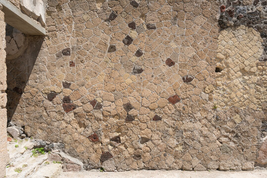 Sunlit ancient Roman opus reticulatum and mixed stone masonry wall standing in historical archaeological ruins under bright sunlight