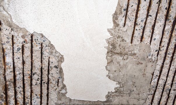 Heavy structural damage and surface spalling on reinforced concrete with visible rows of rusted rebar iron rods amidst crumbling cement plaster
