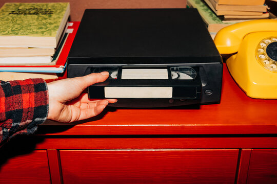 female hand inserts a VHS tape into a VCR, evoking a sense of nostalgia and memories while preparing to watch old home videos from the 90s