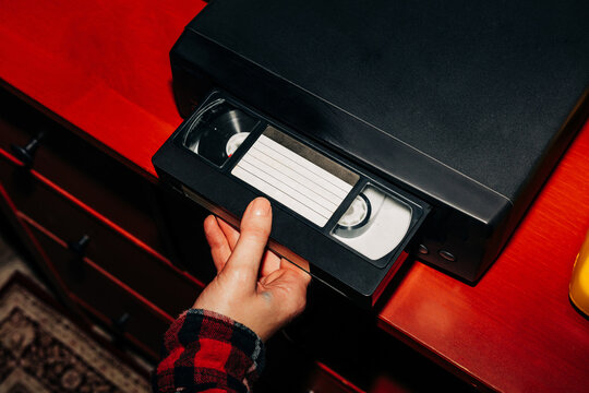 female hand inserts a VHS tape into a VCR, evoking a sense of nostalgia and memories while preparing to watch old home videos from the 90s
