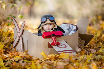 A happy child dreams of traveling in an airplane and plays an airplane pilot. The kid sits in a cardboard plane and pretends to be a pilot in the park in the fall. © sergo321
