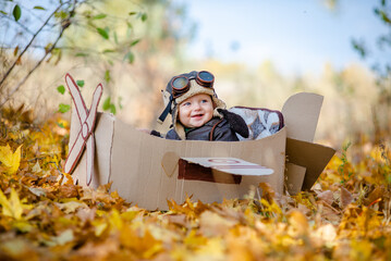 A happy child dreams of traveling in an airplane and plays an airplane pilot. The kid sits in a cardboard plane and pretends to be a pilot in the park in the fall. © sergo321