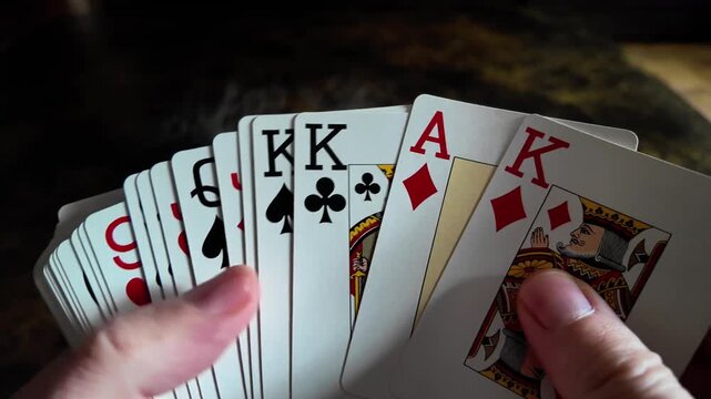 Hands displaying playing cards in slow motion on a wooden table.