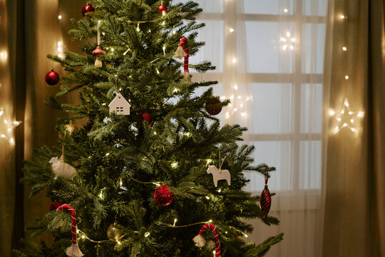 Close up shot of decorated pine tree standing near window during winter holiday celebration. Visual asset suitable for seasonal marketing campaigns and holiday promotions