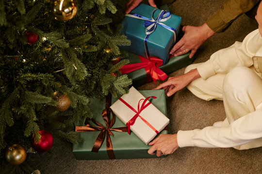 High angle view of Caucasian family placing wrapped gifts under decorated Christmas tree. Scene representing holiday traditions for seasonal retail campaigns