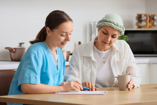 Home healthcare and cancer recovery, nurse consulting with a patient wearing a headscarf during a home visit in a kitchen setting