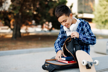 Smiling schoolboy packing books into backpack outdoors © djile