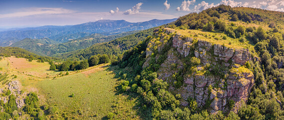 Naklejka premium Rocky cliff face dropping into green alpine meadow - ideal for hiking and adventure tourism campaigns. Balkan highlands destination