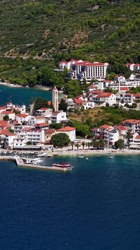 Croatia, aerial view of a coastal town with white houses, red roofs, green hills, and clear blue sea