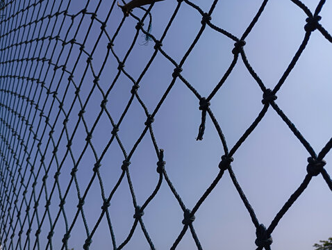 Broken black rope net against clear blue sky