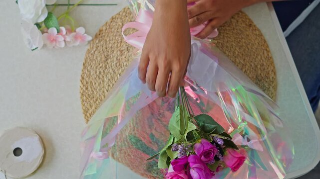 High angle view of florist hands inserting artificial rose and lily stems into wrapped bouquet