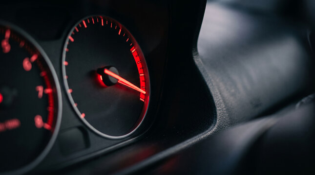Car tachometer needle shows high RPMs in a dark automotive interior