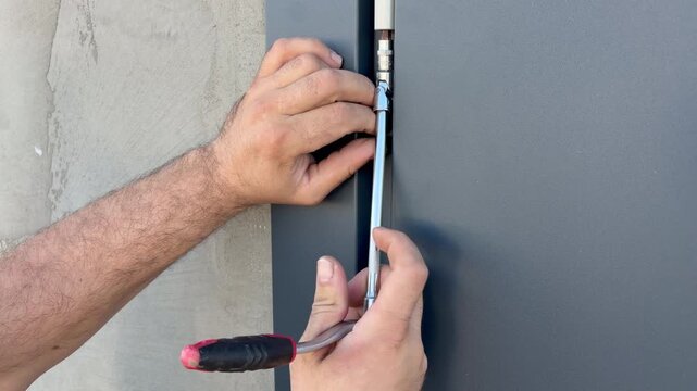 A worker adjusts the hinge of a metal gate using an L-shaped hex key with a T-handle. Hardware installation, gate repair, DIY home improvement, and outdoor maintenance.