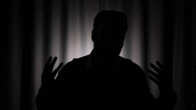 Hidden identity, unidentified person, silhouette, interview. Dark male silhouette against light background. Man is speaking and looking at camera
