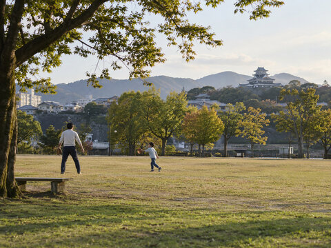 A parent and child playing catch in a Japanese park.