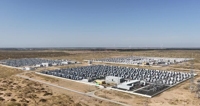 Orbiting aerial drone footage of energy storage station, a large containerized battery storage facility surrounded by sand dunes and transmission towers, Dengkou county, Inner Mongolia, China