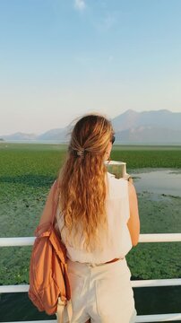 Tourist girl enjoying a boat ride landscape of Lake Skadar, spanning Montenegro, Albania. green plants leaves specifically water caltrop, Trapa natans, float cover water surface. sunset sky mountains