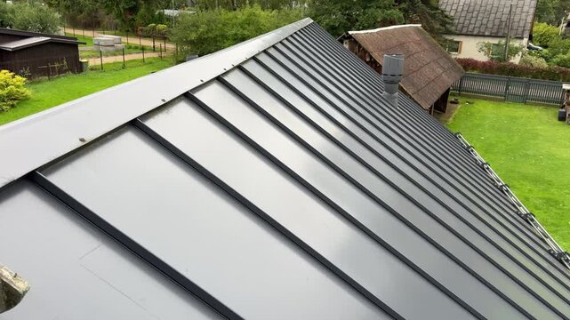 Dark grey profiled metal roof sheets with standing seams. Roofing materials, building envelope, durable cladding, construction, home renovation, weatherproofing.