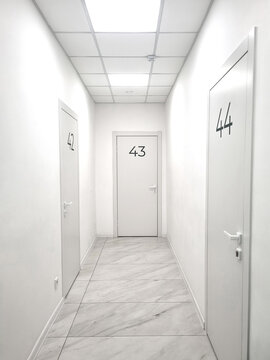 Vertical perspective shot of bright empty hospital clinic corridor with white walls tile floor closed doors numbered forty two forty three and forty four bright ceiling lighting interior