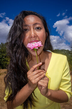 Portrait of young Asian woman holding delicate pink flower outdoors