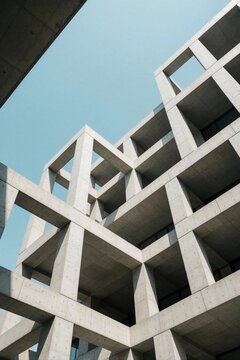 Low angle view of modern concrete building with geometric shapes. Minimalist architecture features grey structure against clear blue sky. Contemporary urban design shows symmetrical grid pattern,