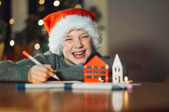 Smiling boy in Santa hat writing a Christmas letter indoors