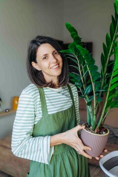 A smiling woman holds a green houseplant in a flower pot at home