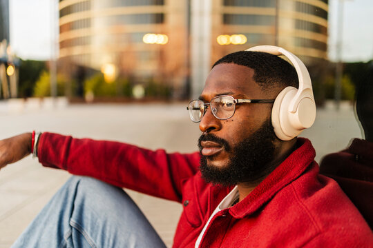 Man relaxing outdoors with headphones and red jacket in urban city