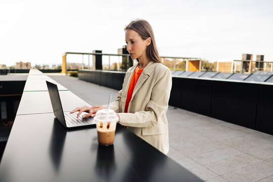Woman working remotely outdoors with laptop and coffee