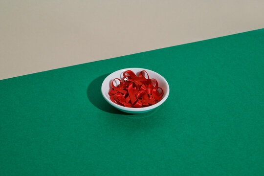 Red HIV awareness ribbon in a white bowl on green background