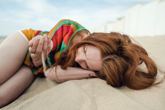 Redheaded woman lying on the beach, with sand trickling through her hand