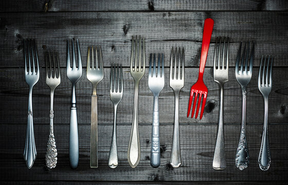 Row of different silver forks and a red plastic fork on wood