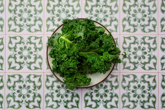Fresh curly kale sits on a plate over green patterned tiles