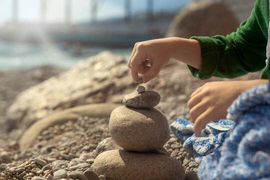 A boy stacks a rock on a sunny pebble beach